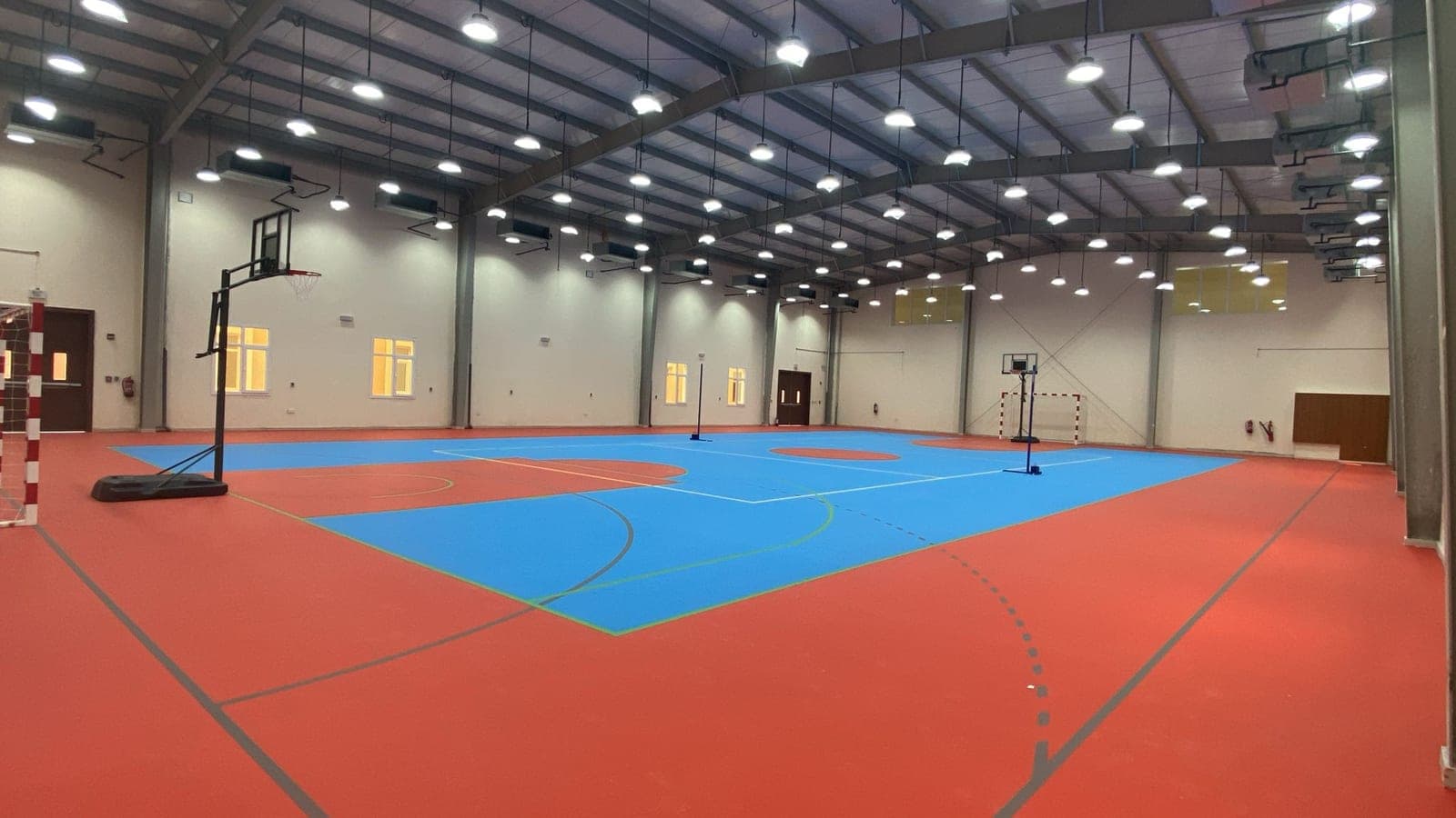 Inside the sports hall, a marked court under the steel portal frames and rows of high bay lights